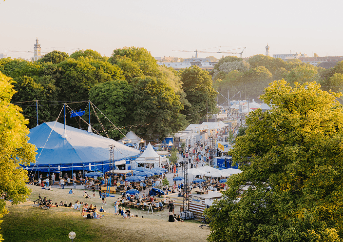 Luftaufnahme des Tollwood-Festivals im Olympiapark München bei Sonnenuntergang.