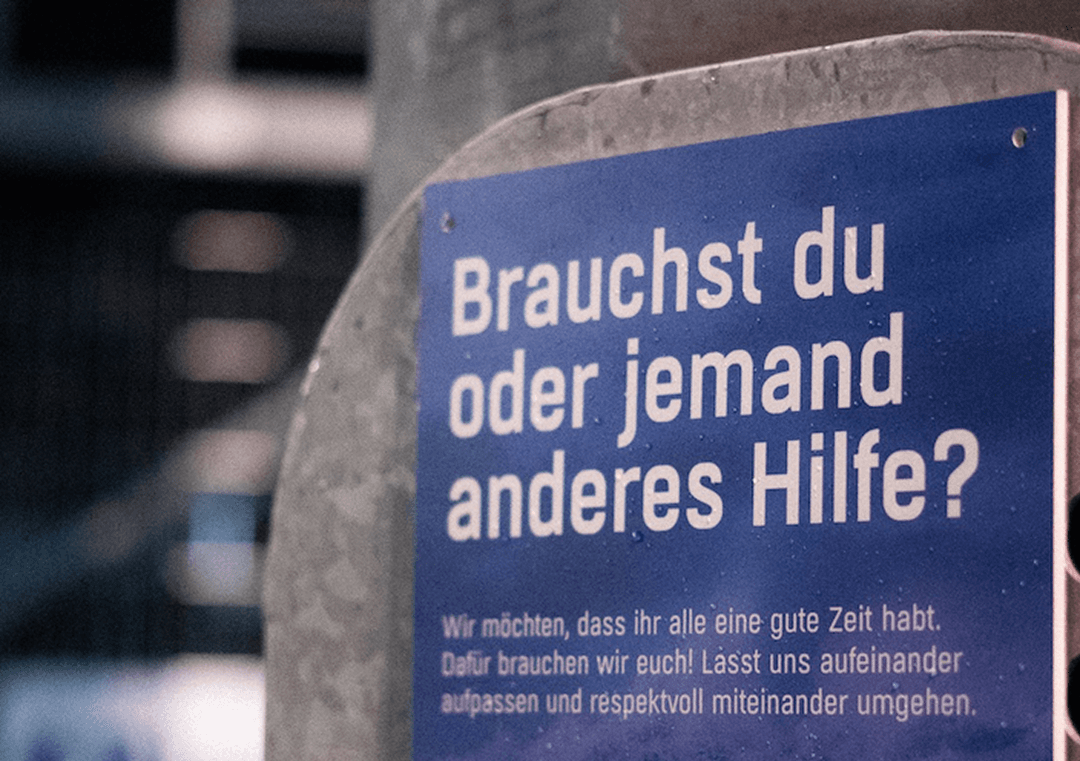 Blaues Schild mit der Aufschrift: „Brauchst du oder jemand anderes Hilfe?“ und Hinweis zu gegenseitigem Respekt.