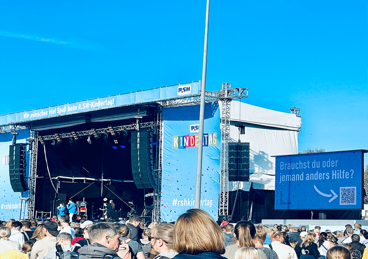 Stage at the RSH-Kindertag with audience, banner text: „We wish you a lot of fun at the R.SH-Kindertag“, help hint on canvas.