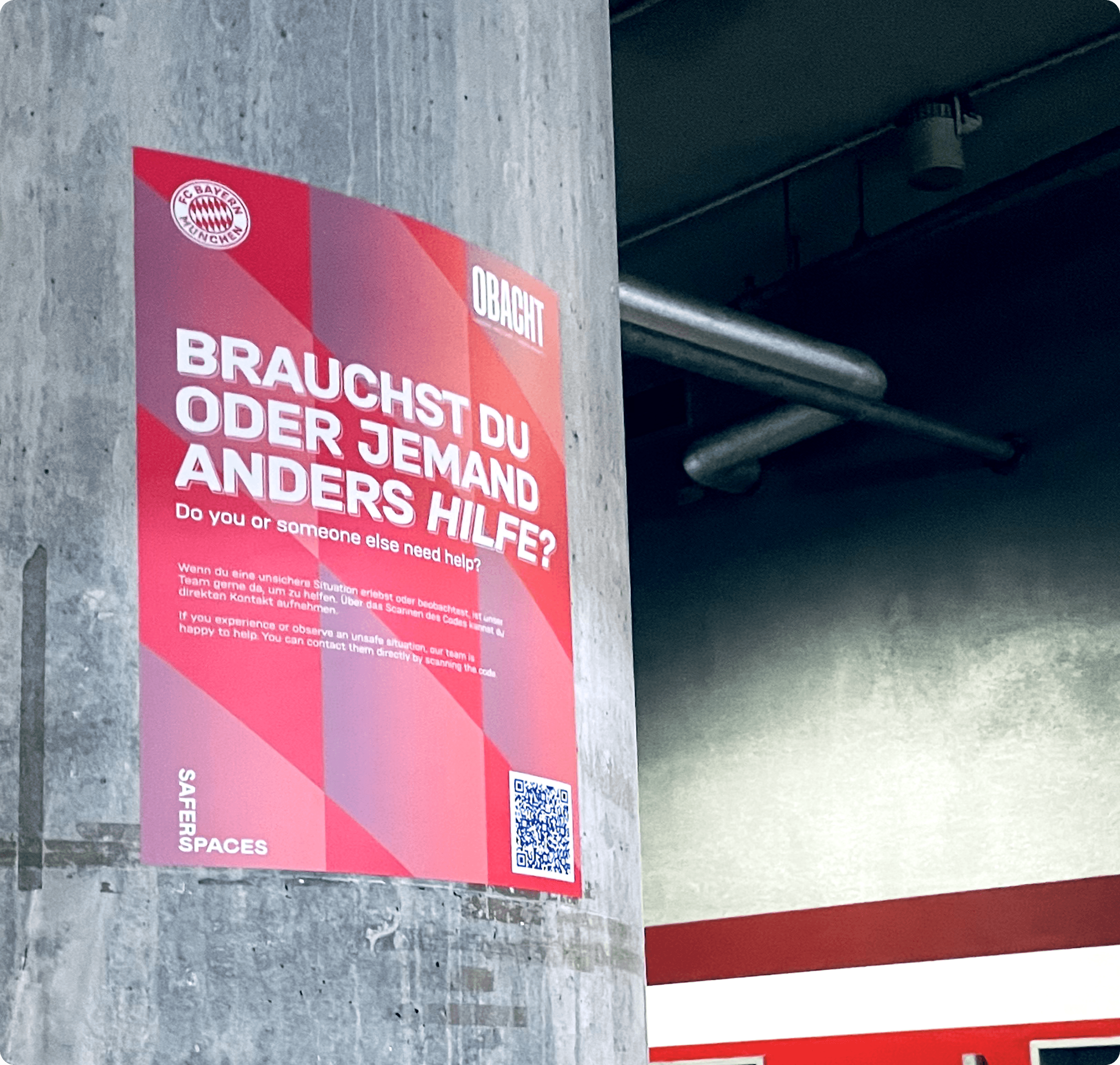 Rotes Plakat des FC Bayern München an einer Säule mit Text: 'BRAUCHST DU ODER JEMAND ANDERS HILFE?' und QR-Code unten rechts.